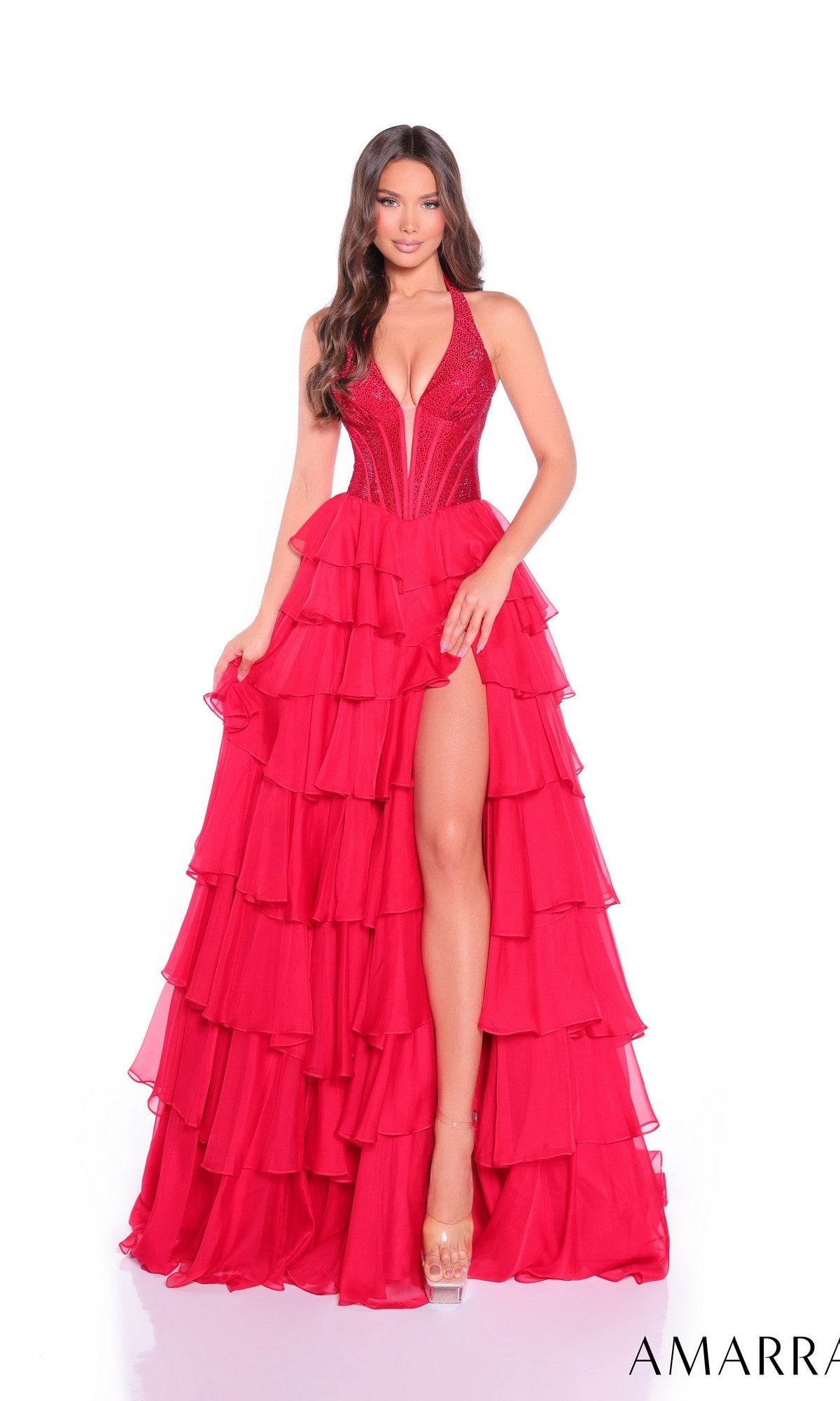 A woman poses against a white background wearing the Amarra 89287 long prom dress—a vibrant red gown with tiered ruffles, embellished corset bodice, deep V-neck, and high slit.